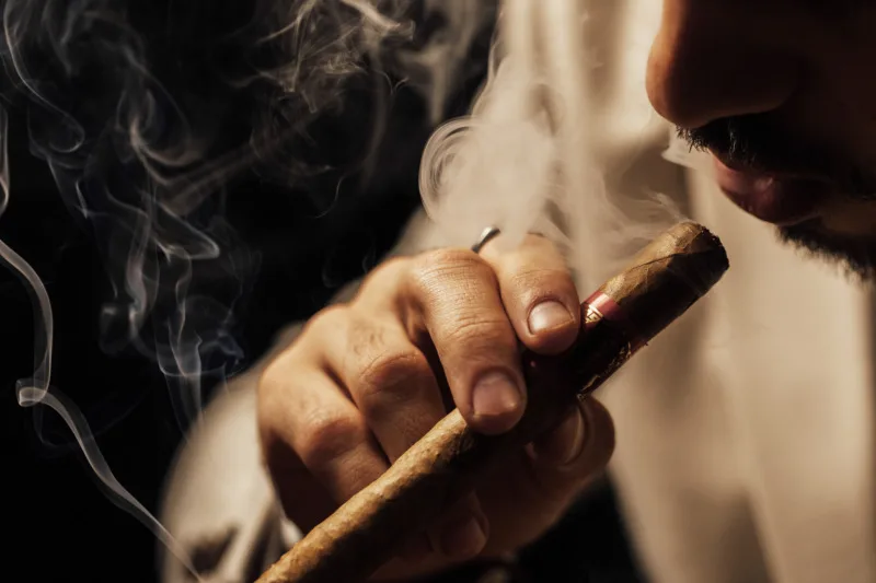Close-up of a hand holding a lit cigar in drifting smoke