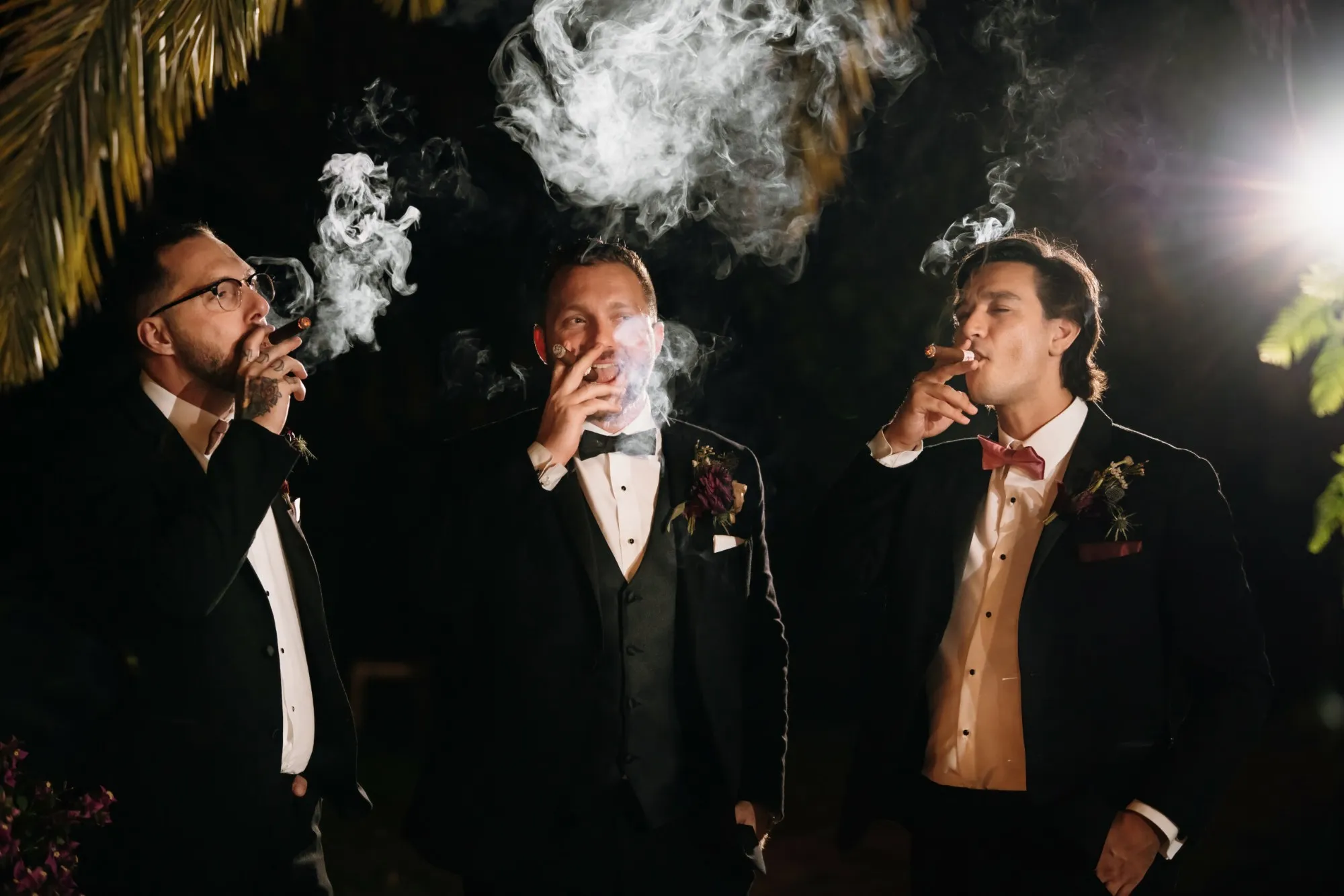 Three men in tuxedos smoking cigars at an evening party